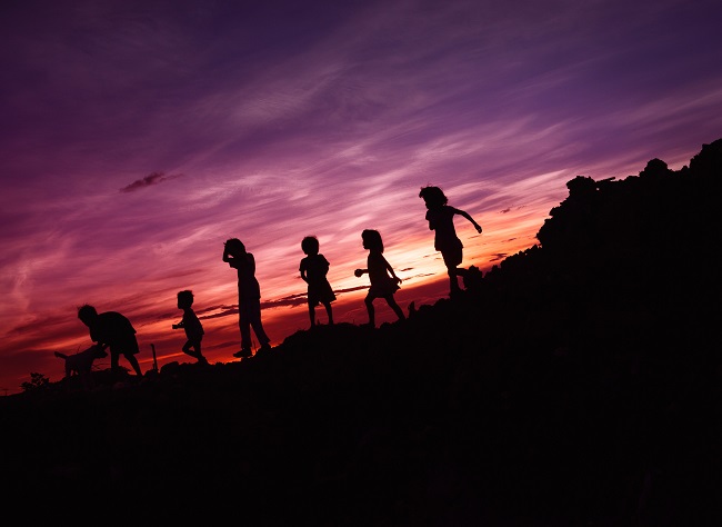 Several children are seen in silhouette against a pink sunset. they appear to be playing on rocks. God created man to be His children and had to become man in order to save them.