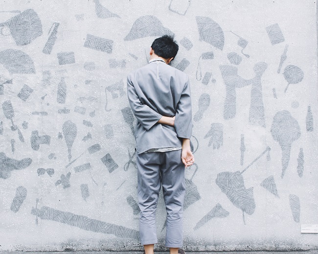 A man in a pale gray suit stands facing towards a gray-painted wall with his hands behind his back. His head leans up against the wall. If you need help with grief recovery, God can provide that help.