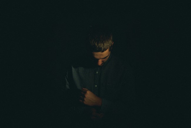 A man stands in the dark with his head bowed and a fist in front of his chest, as if he is holding in pain. God will bring you out of the darkness of grief, if you allow Him to. A man stands in the dark with his head bowed and a fist in front of his chest, as if he is holding in pain. God will bring you out of the darkness of grief, if you allow Him to.
