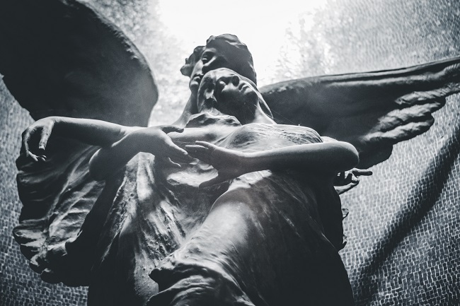 A statue, seen from a low angle, depicts two angels sitting together with their eyes closed in reverence. What will we look like in Heaven? We will look much like we do now.