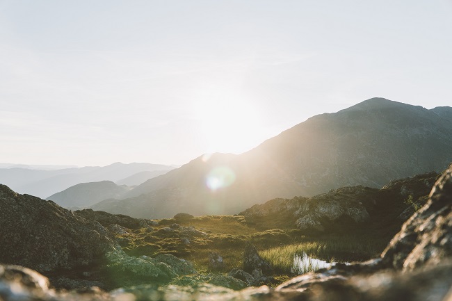 A beautiful landscape shot of mountains and fields as the sun rises from behind the mountains. We can be sure of health and vitality in Heaven, even if our bodies on Earth are currently not healthy.