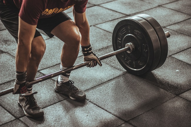 A weightlifter stands behind barbells with his hands gripped onto the bar, ready to lift in any moment. Will we have beautiful sculpted bodies in Heaven? 