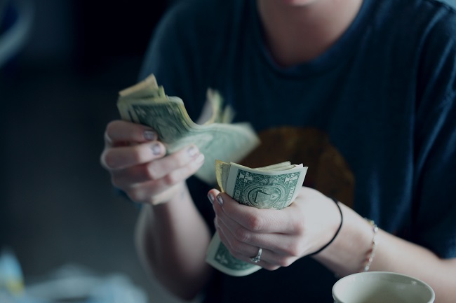 A woman holds up a wad of cash as she counts out bills. Can building wealth and having lots of money really make us happy? 