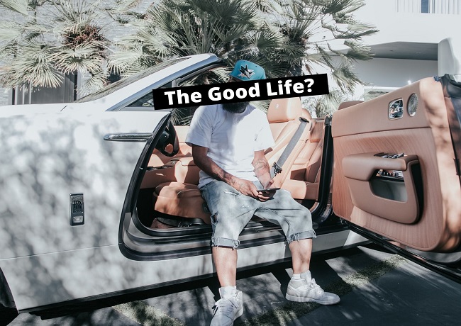 A Man sits in his expensive-looking car, with a mobile phone in his hand, surrounding by palm trees. He looks wealthy, but is he rich in his soul?