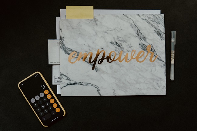A mobile phone with the calculator app open sits on a dark desk next to a folder with the word 'Empower' written on it in gold. Can giving bring us true joy and happiness? God thinks so!