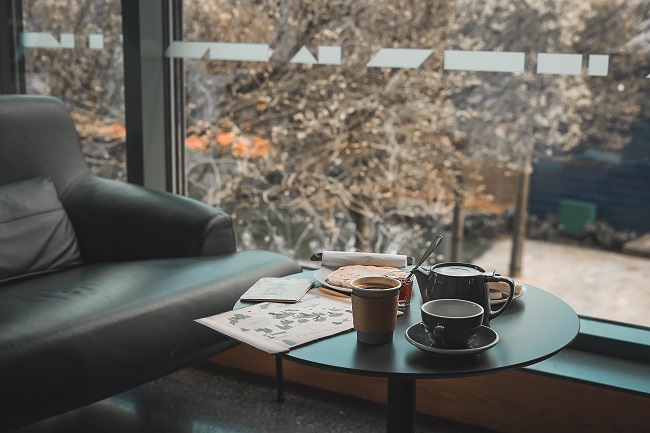 An empty green leather chair sits beside a large window. A small table in front of the chair contains coffee cups and paperwork.