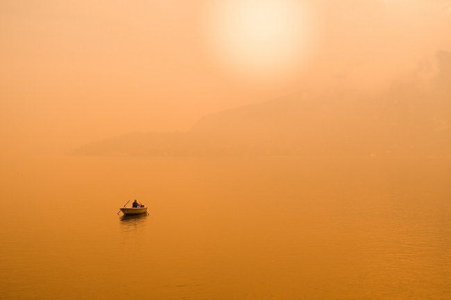 A small boat is seen way out on a lake that is bathed in hazey orange light.