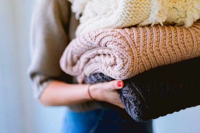 A woman holds a small pile of thick blankets for donation.