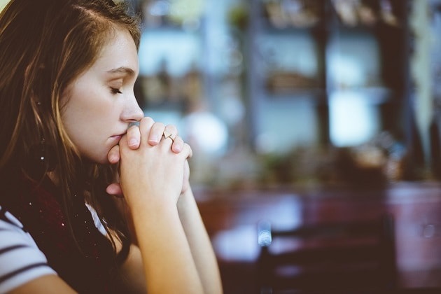 A young woman prays to God in a sitting position, inside a church.