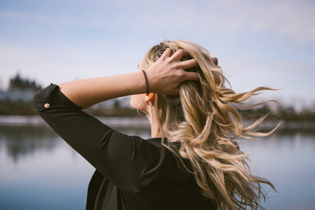 A young woman holds her head with joy, stood beside a refreshing lake, demonstrating God's love for us all