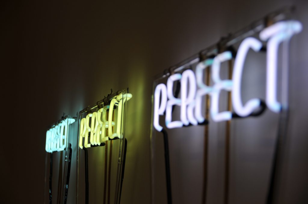 Three neon signs of the word 'perfect', demonstrating God's love for us all