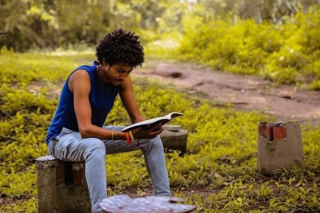 Young man sat on a log in a park, reading. Encouraging quiet time.