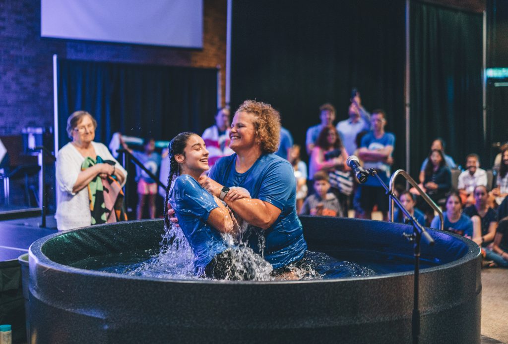 A teenage girl emerges from baptism waters at her church. She is smiling.