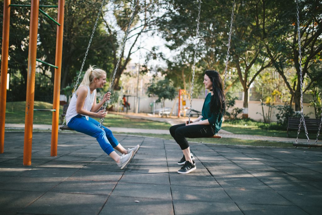 Young ladies hang out and chat about faith on park swings.