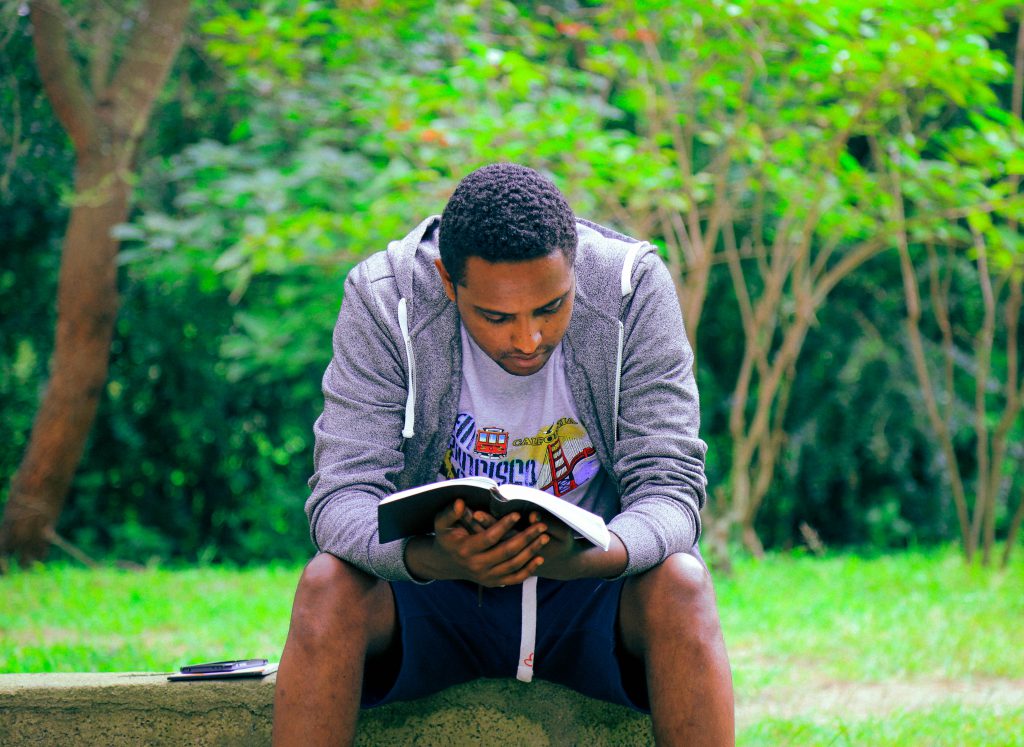 A man in deep study of his Bible outside in a lovely countryside setting.