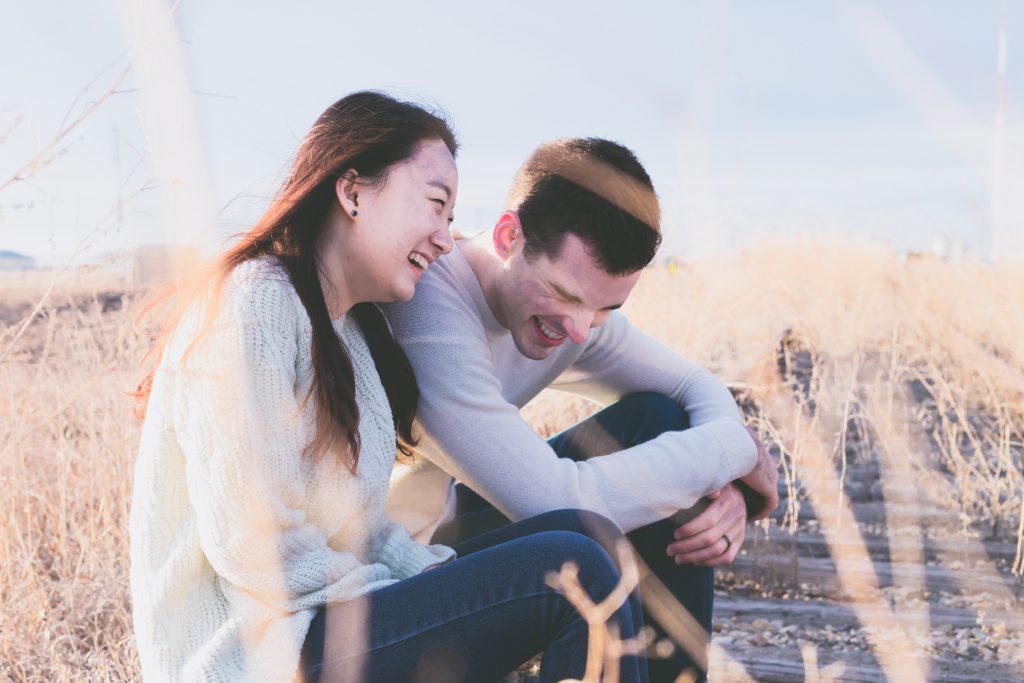 A man and woman laugh together in a field on a sunny day. Best devotionals for new believers, one year devotional for men and women.