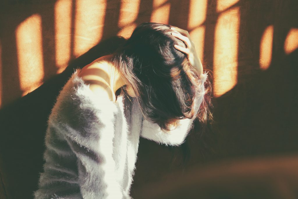 Sin will be forgiven by our loving God. A young woman in a white sweater covers her face and bows her head.