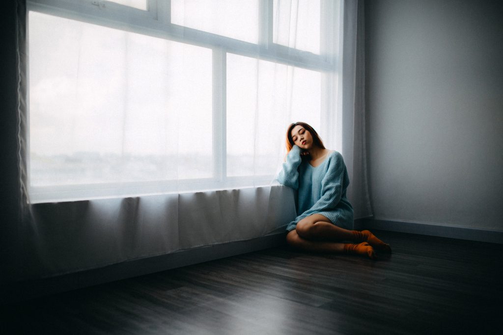 A sad girl sits alone by a window, on a wooden floor. This testimony is upsetting but God saves.