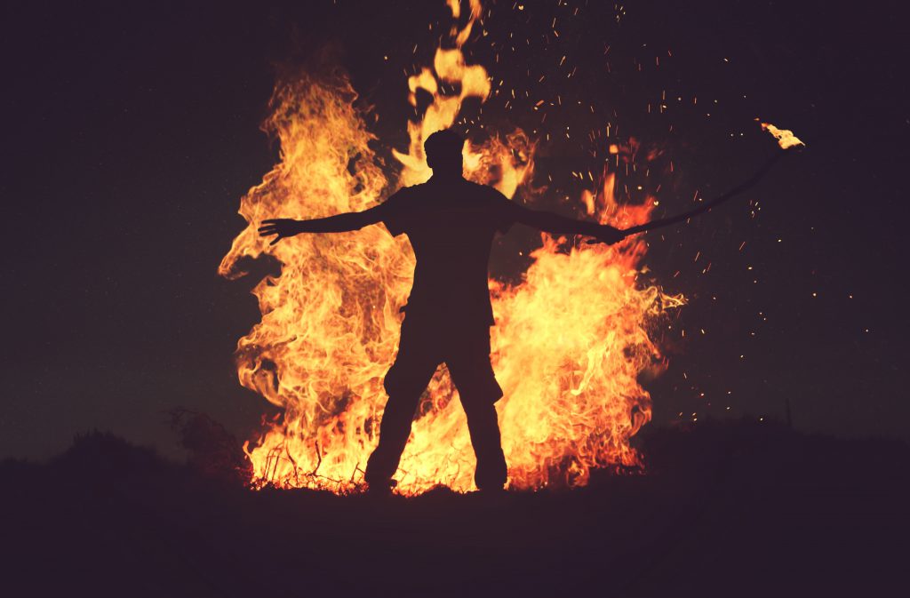 Man stands in front of a very large fire he has started. Aggression is part of this testimony.