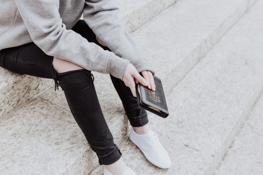 Someone holds a Bible while sitting on stone steps. God can help you with avoiding sin.