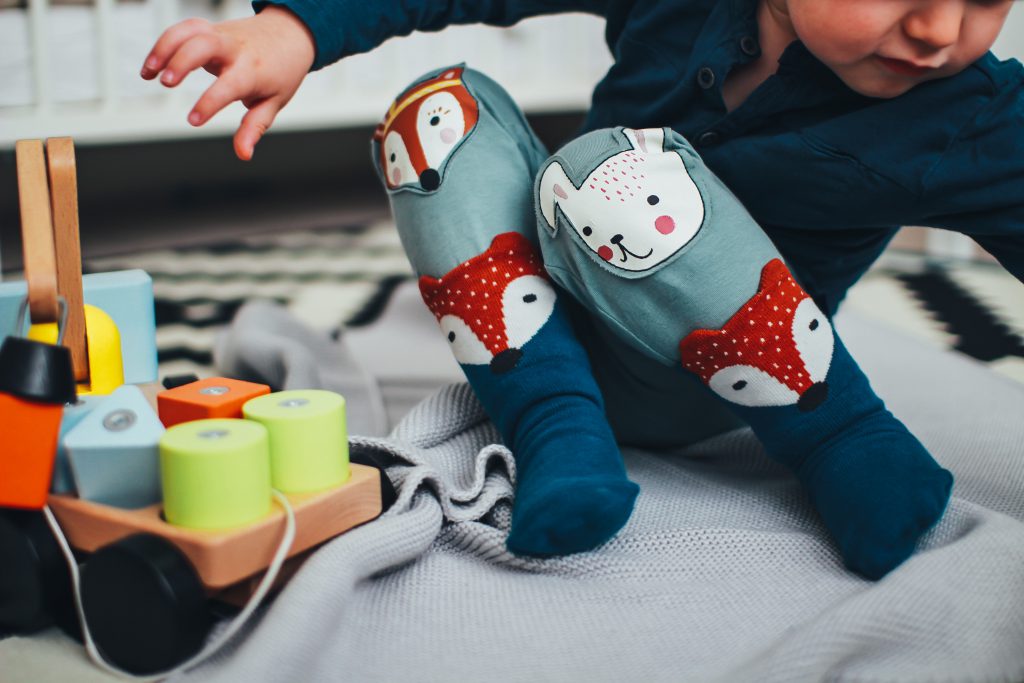 A young child in colorful stockings sits on a blanket and plays alongside a wooden toy with blocks in various shapes. Children should be taught about giving, as Jesus gave to us, as well as receiving at Christmas.