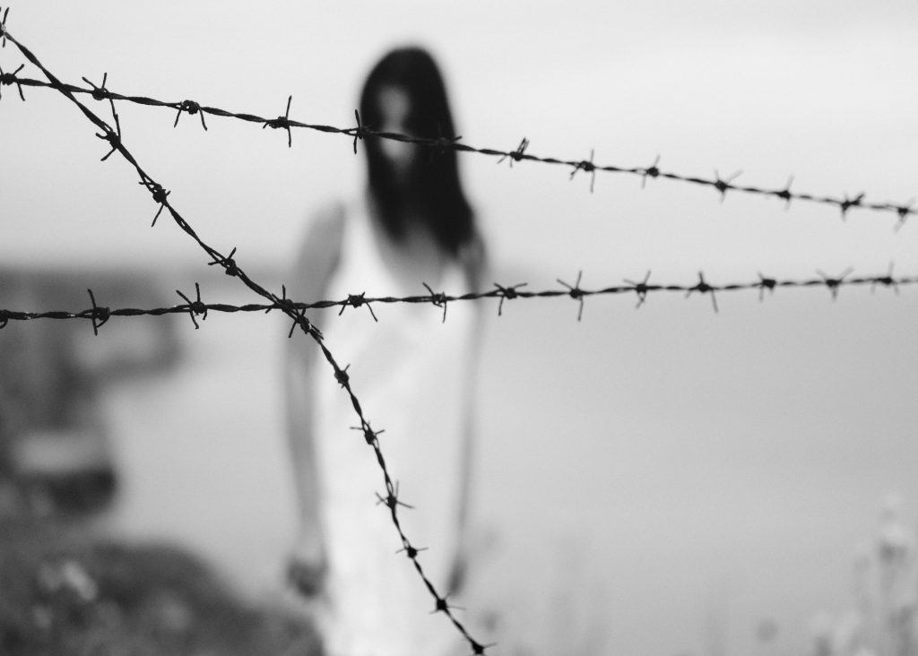 Why does God allow suffering in the world? Image of a woman behind barbed wire, black and white.