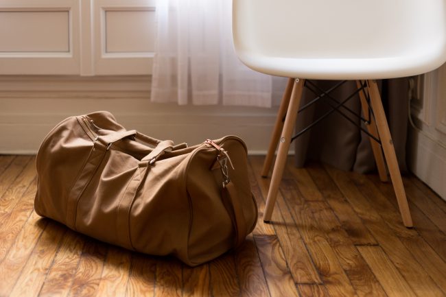 A packed duffel bag sits on a wood floor next to a white and natural wood chair. Forgiveness can be very difficult to achieve, but we are called by God himself to do it.