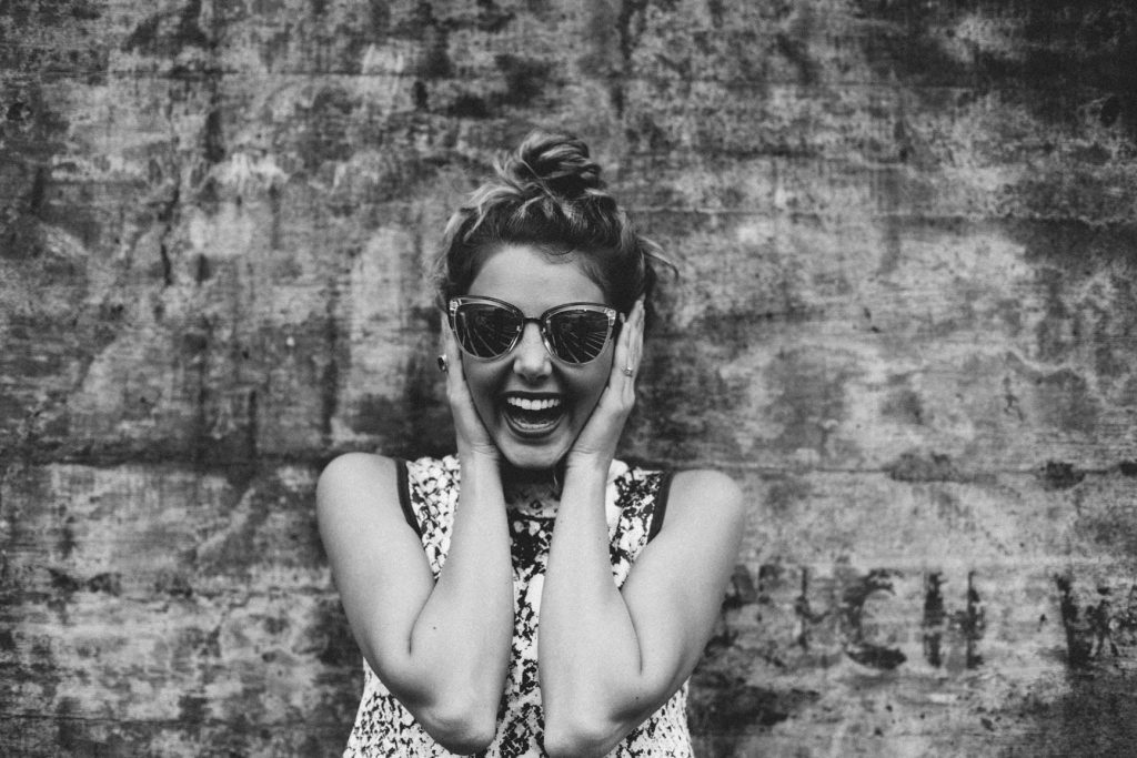 A young woman in sunglasses laughs with glee as she shares her own story.