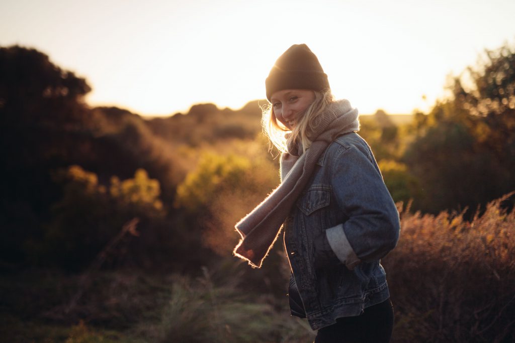 Image of a woman outside in a field at sunset. She is wrapped up in a warm hat and scarf. Gods grace can allow us the freedom to make a fresh start in the new year.