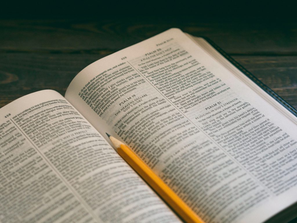 A Bible sits open on a wooden table, with a yellow pencil sat in the middle of it. your Bible can help you navigate life and answer all your questions.