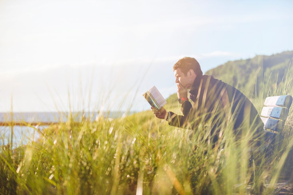 A man sits on a bench on a cliff over looking the sea. He is reading his Bible in search of answers to his big questions. The HelpFinder Bible can help you find those answers quickly.