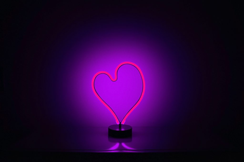 Lament says we can have an intimate and even more loving relationship with God. A neon purple heart lights up a bare wall behind it in the dark.