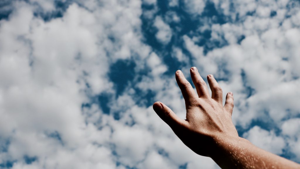 Lament prayers offer us relief. A hand reaches up to a blue sky with clouds.