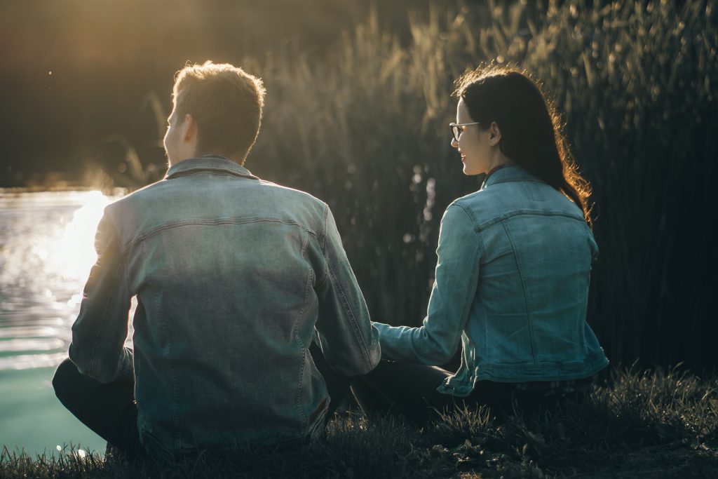 A couple sit holding hands beside a small river with the sun gently lighting them. How can we improve our relationships? By improving ourselves, with God's help.