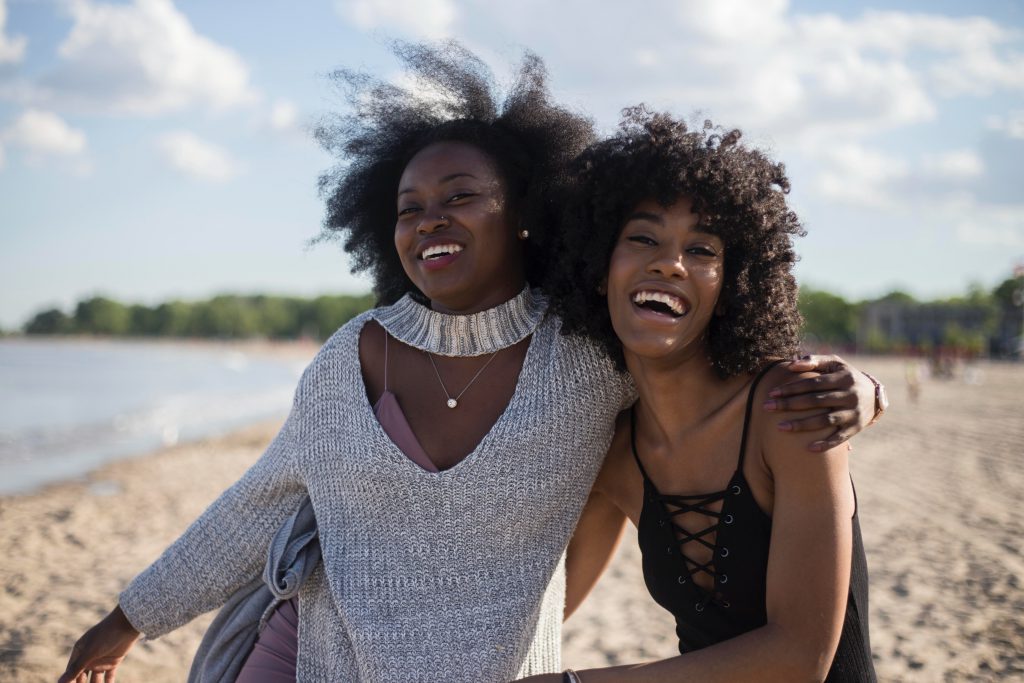 two female friends laugh and hug on a beach on a sunny day. These principles of looking within ourselves to improve our relationships works for family and friends, as well as spouses.