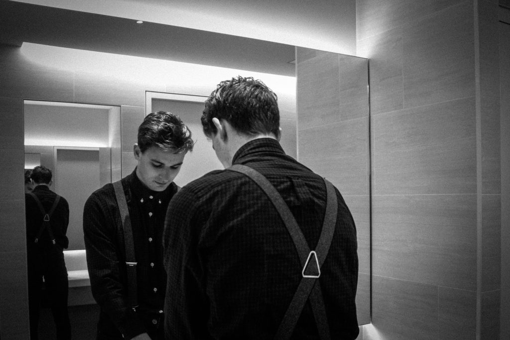 A young man dressed for a night out stands in front of a smart bathroom mirror with his head bowed as he looks down. Reading the Word of God everyday can help us to start relying on God's promises.