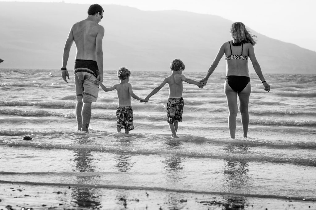 A family with two young boys hold hands and wade into the sea. Trusting in God's promises helps us to relax, to rest, in the knowledge that God has got this for you!