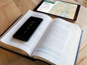 Pictured is a copy of the Filament Bible, sat open on a table with a mobile phone showing the accompanying app, and a tablet also showing the app.